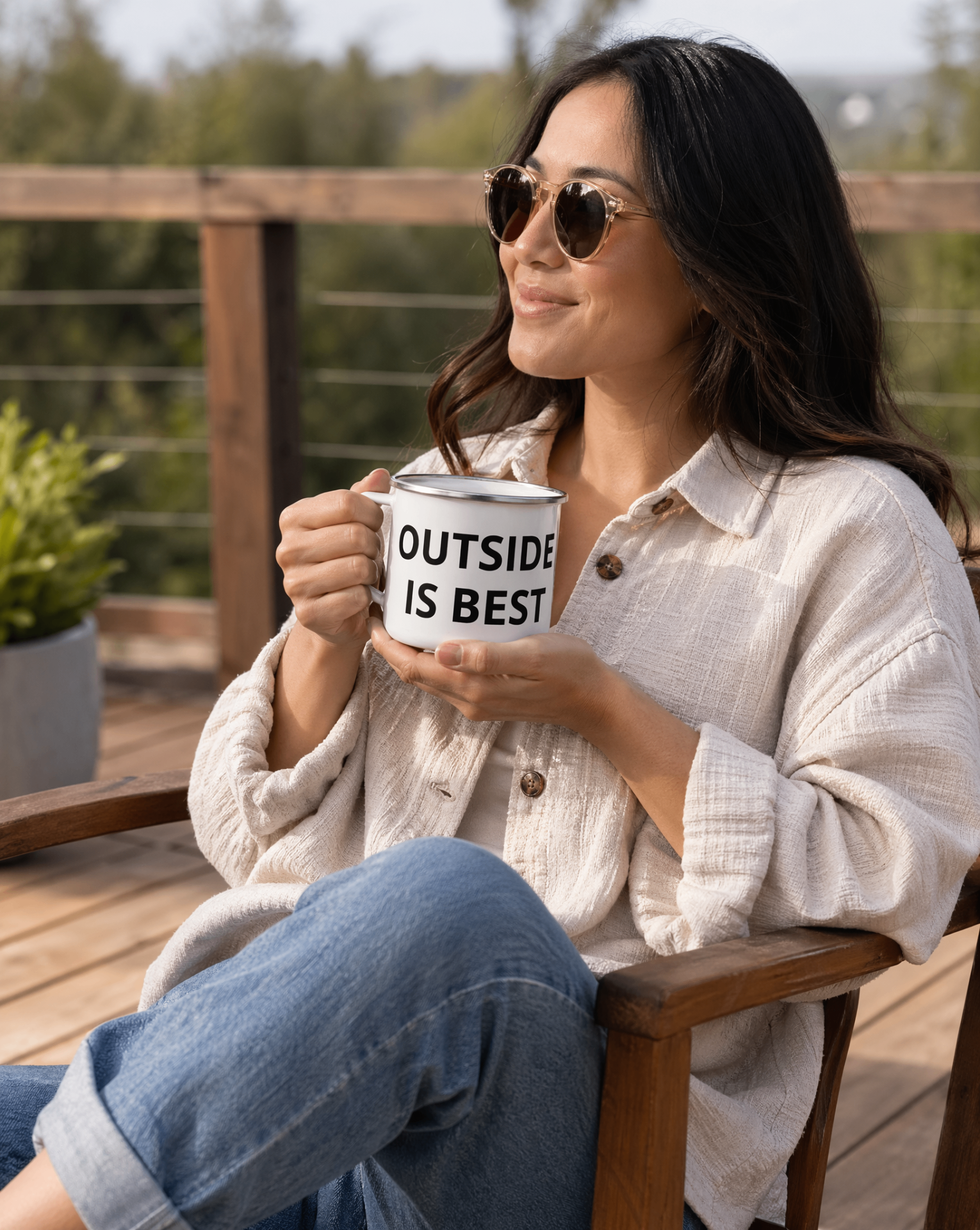 Smiling woman in sunglasses on a wooden deck holding the Outside Is Best enamel mug